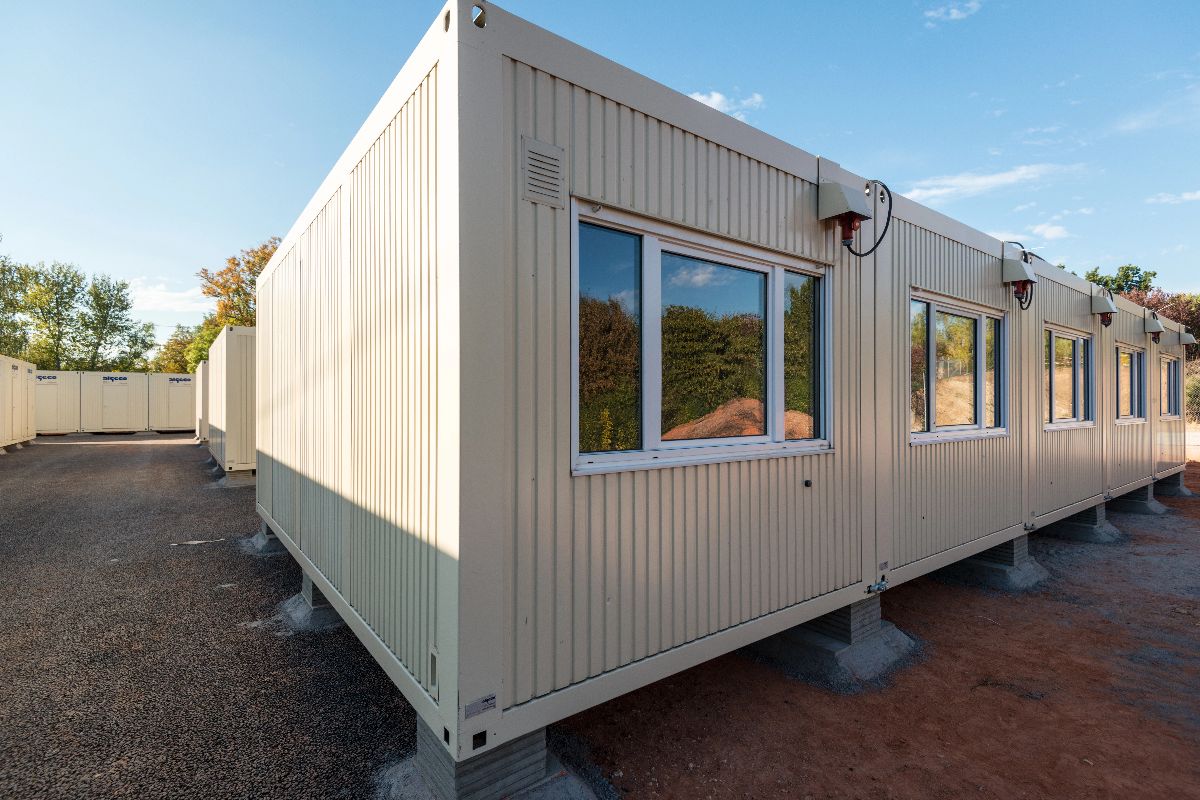 Long prefab mobile office building with windows, doors, and exterior drainage along a site pathway