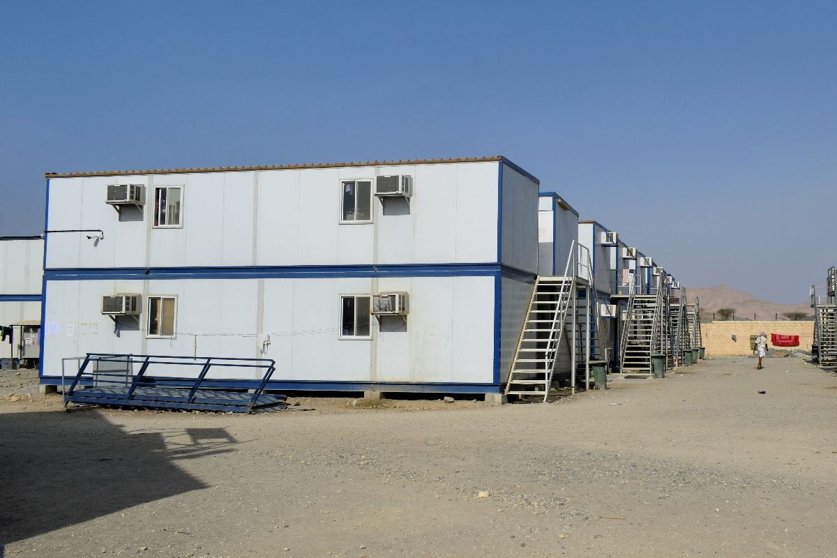 Row of white prefab container units with air-conditioning systems installed at a construction site