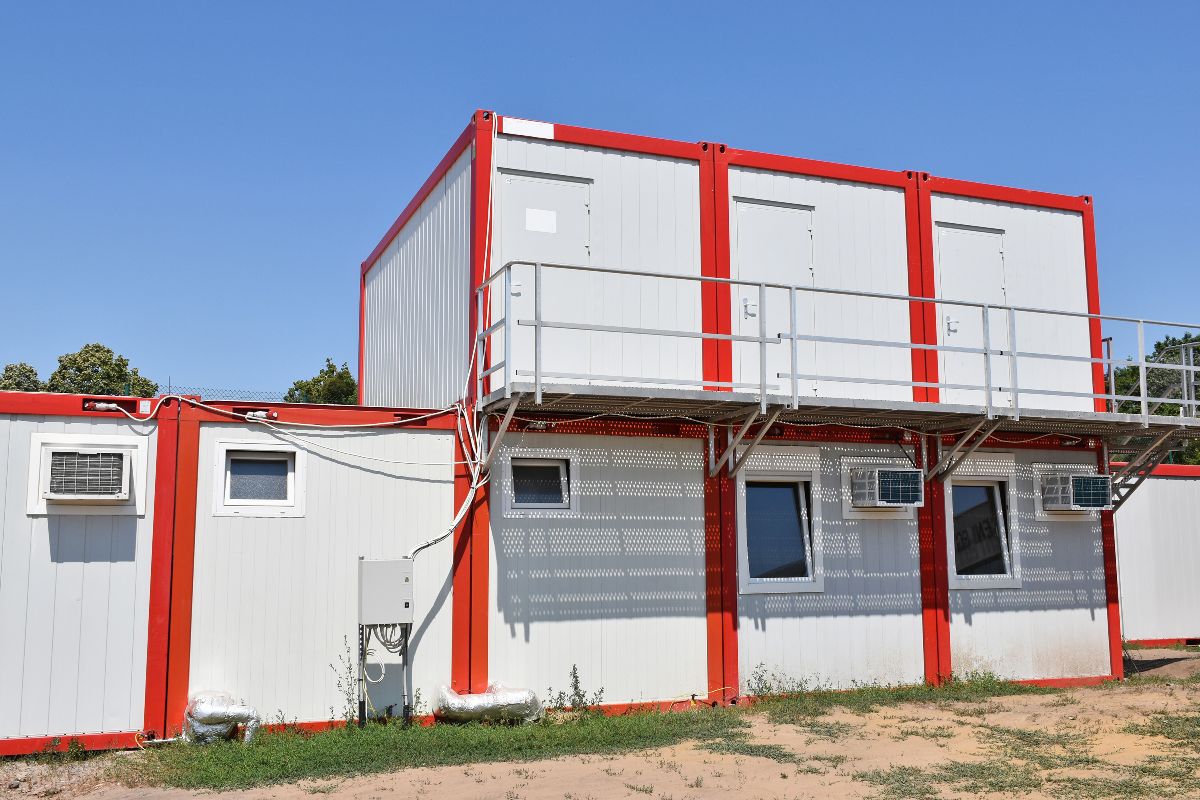 Two-storey red and white modular office units with exterior walkway, stairs, windows, and air-conditioning