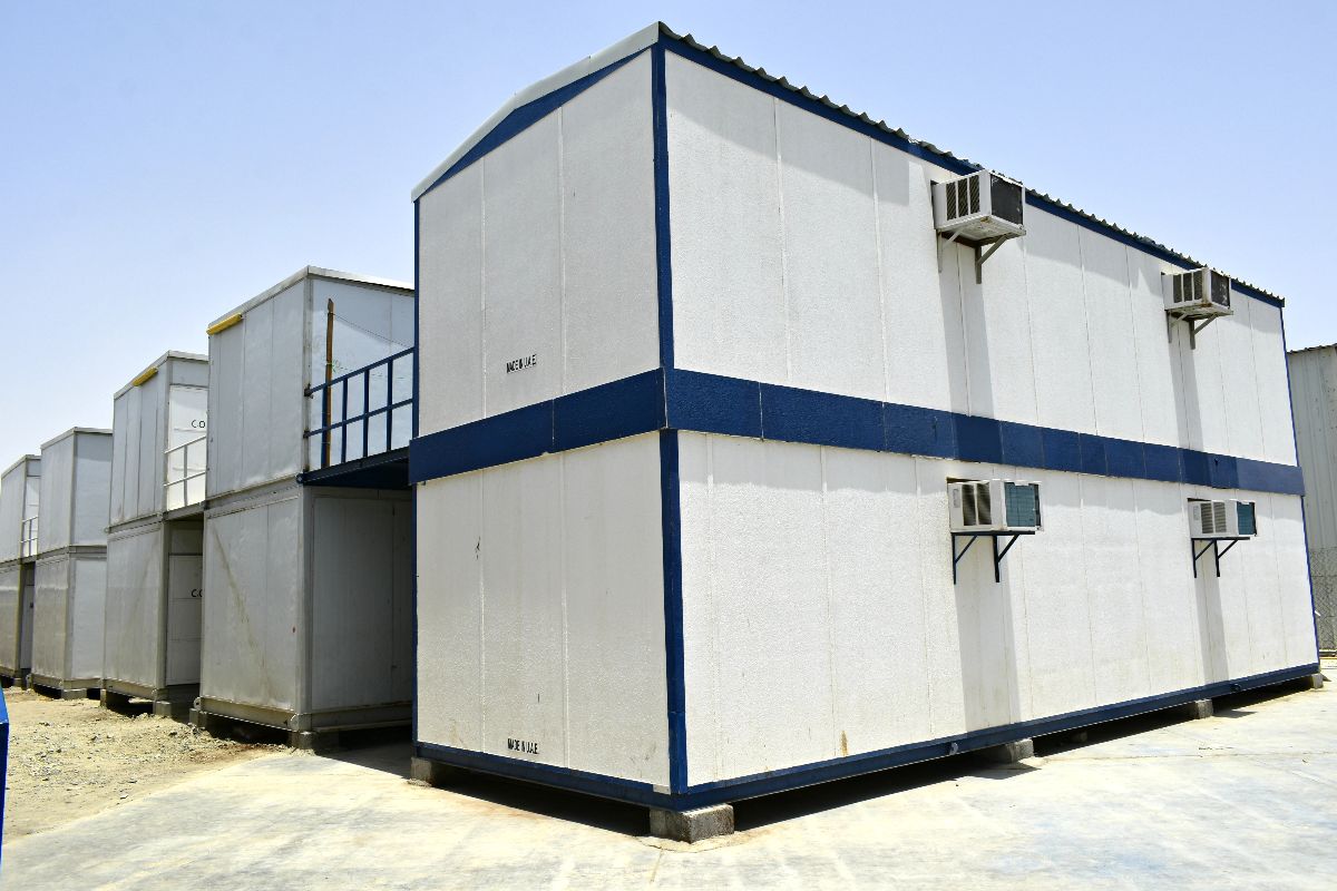 Two-storey prefab office building with exterior staircase, blue trim, and multiple air-conditioning units
