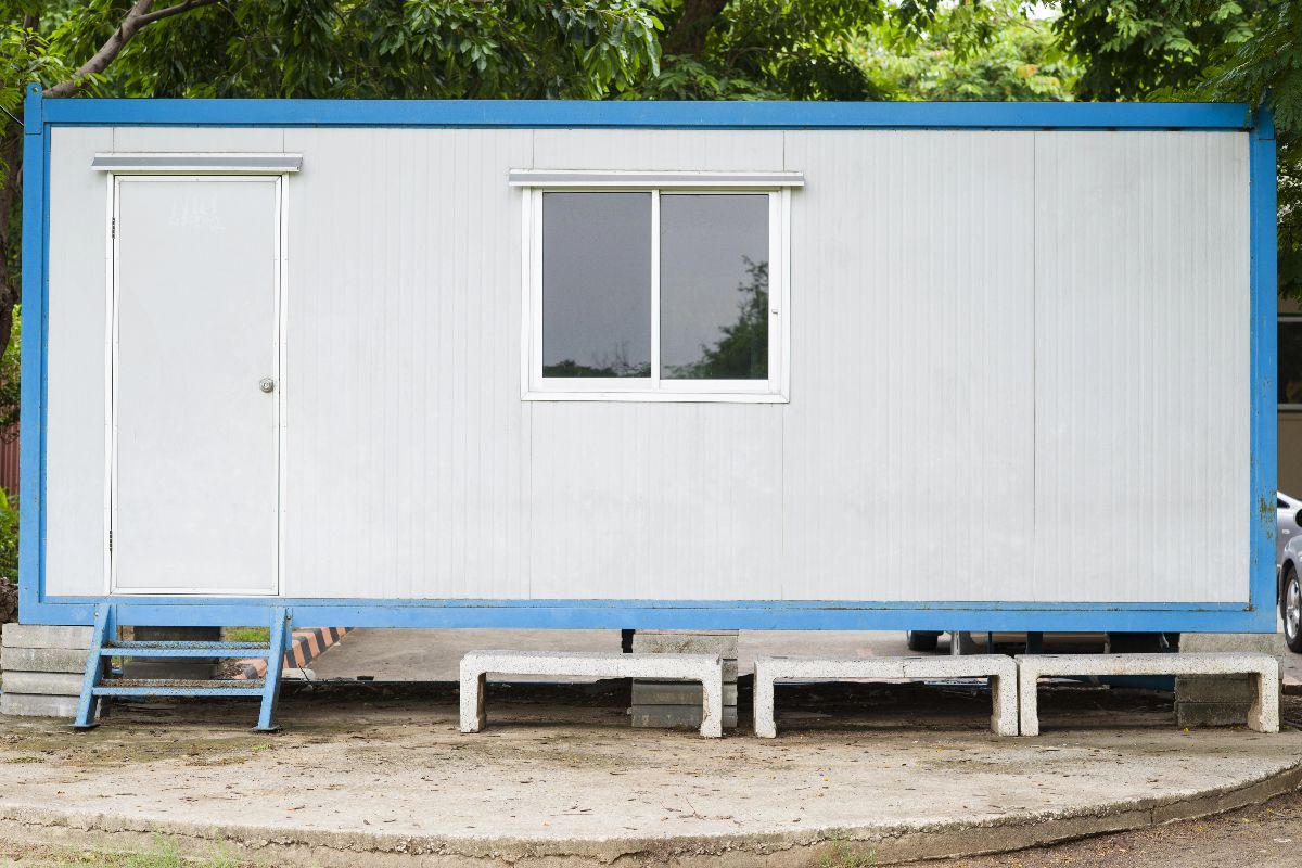Single-level blue and white prefab office container with a door, window, and raised block foundation