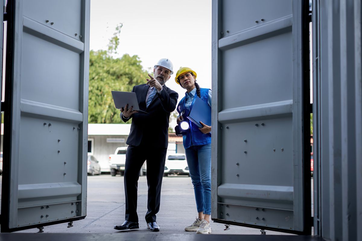 Logistics professionals inspecting a container facility while reviewing plans on a laptop and clipboard.