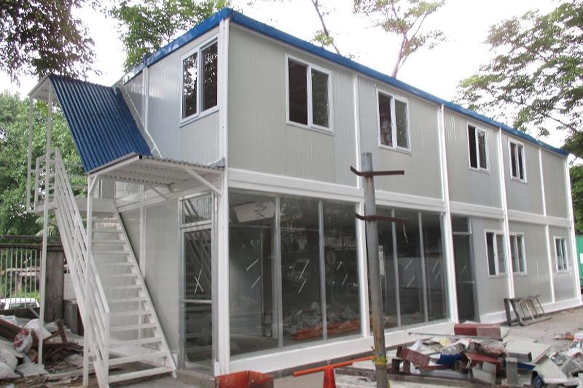Two-story prefab container office building with multiple windows, glass panels, and an exterior staircase