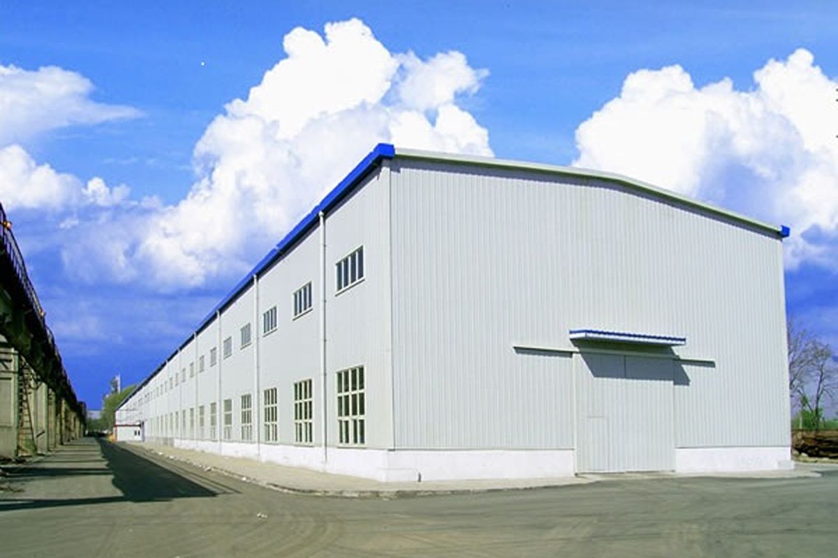 Large prefab industrial building with metal exterior panels and multiple windows under a clear sky
