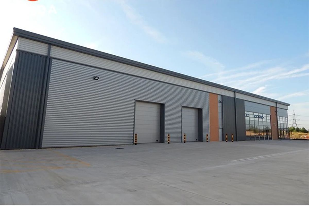 Large prefab industrial building with metal wall panels, multiple doors, and a spacious paved exterior