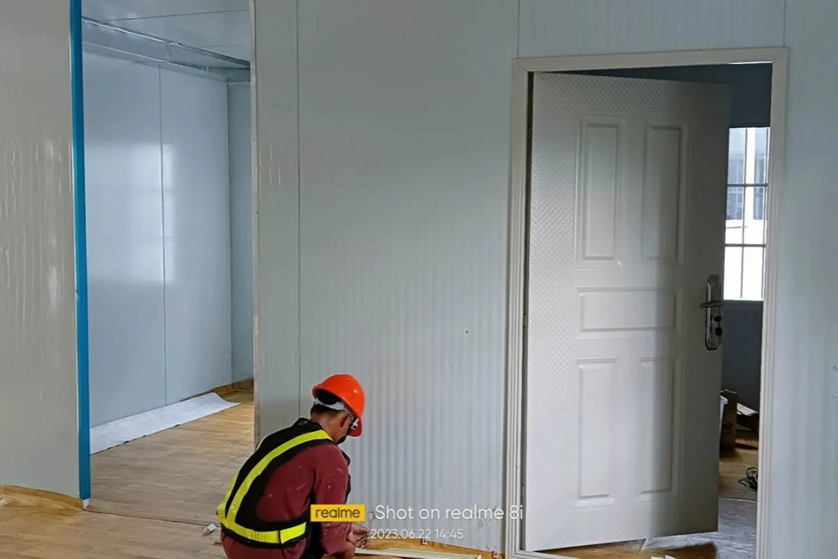 Worker installing interior finishes inside a prefab rental unit with insulated wall panels and partitioned rooms